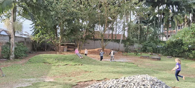 Crianças brincando livremente no pátio gramado com monte de terra e árvores