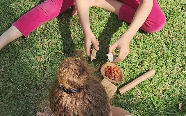 Crianças brincando na grama com sementes e elementos naturais